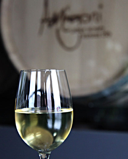 A glass of white wine placed in front of an Amigoni wine barrel during a private tour.