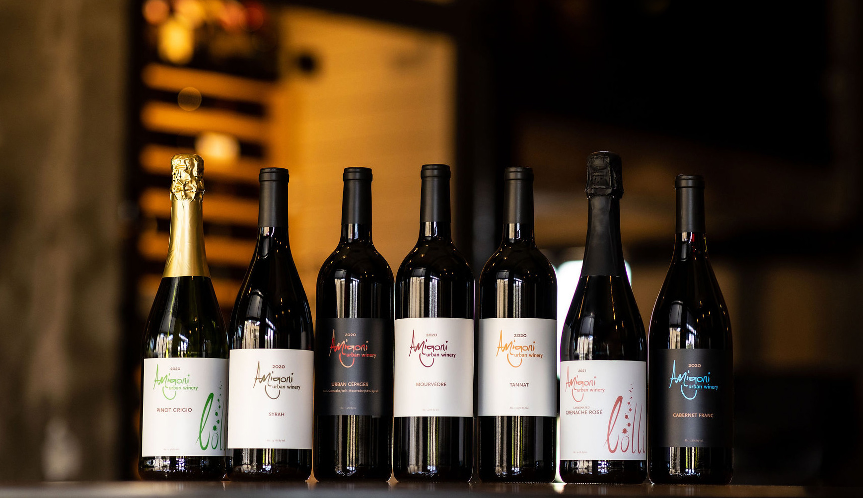 A lineup of six wine bottles from Amigoni Urban Winery, featuring various labels including Pinot Grigio, Syrah, Urban Cépages, Mourvèdre, Tannat, and Cabernet Franc.