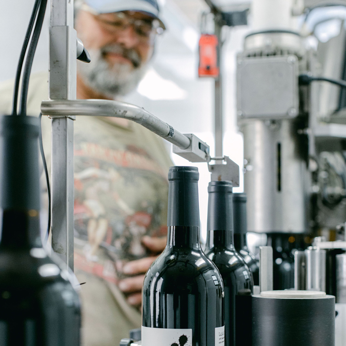 A man oversees the labeling process of wine bottles on an assembly line at a winery.