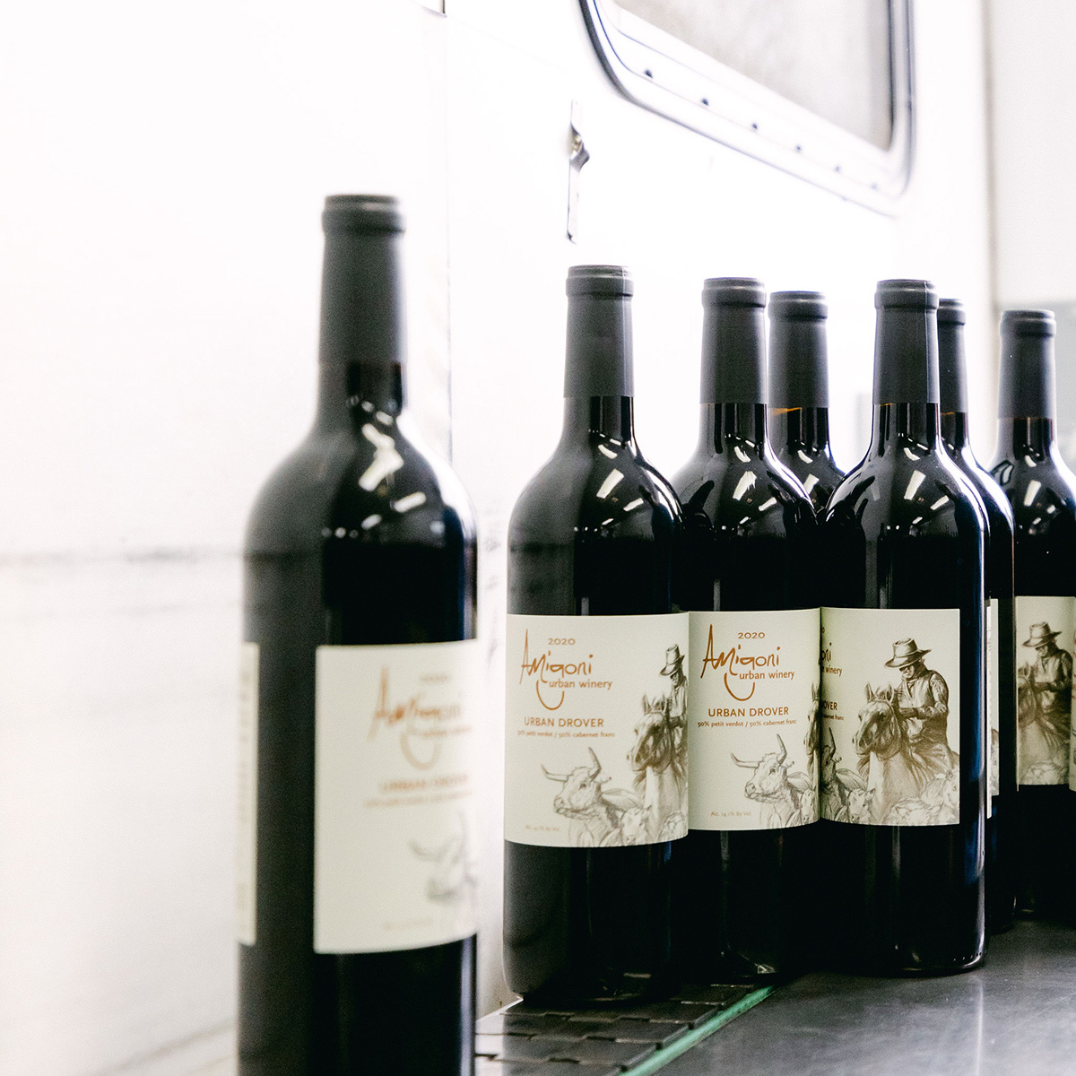 A lineup of Amigoni Urban Winery's Urban Drover wine bottles on a conveyor belt, freshly labeled and ready for packaging.