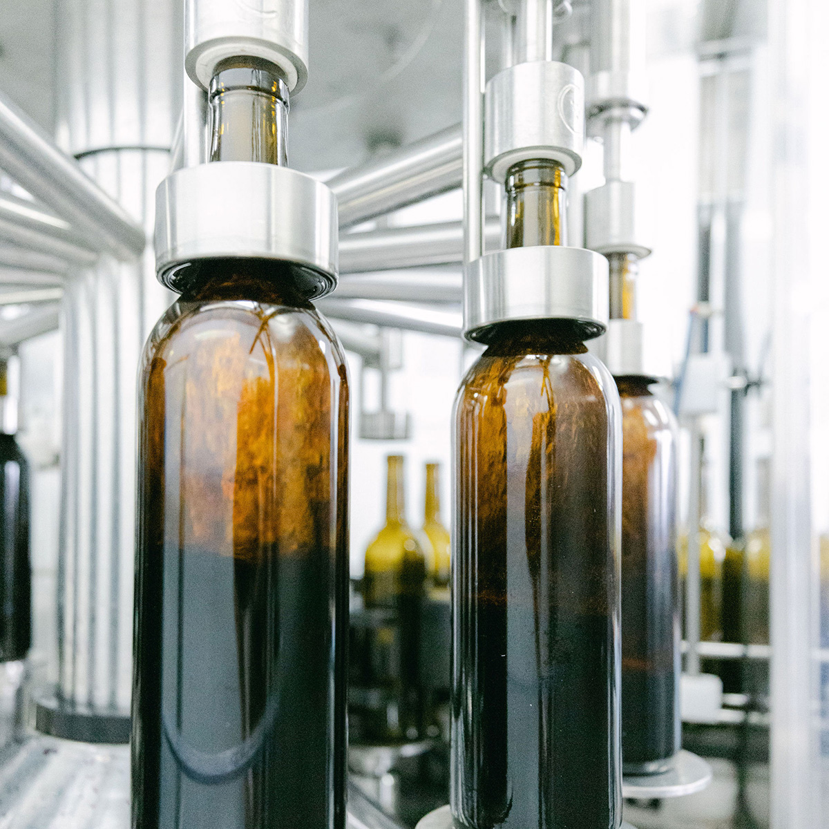 A close-up shot of a wine bottling machine, with several bottles being filled with red wine.