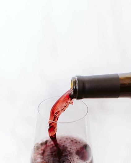 A close-up shot of red wine being poured from a bottle into a wine glass, with a clean, white background.